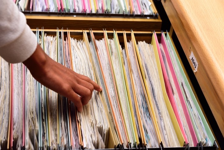 A data scientist looks through unstructured data in the form of hanging files in a filing cabinet